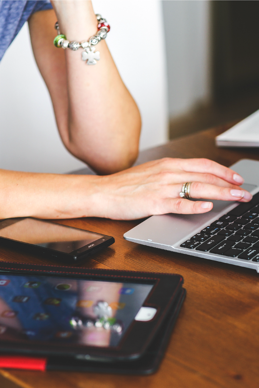 Cropped view of woman working on laptop. Laptop sits on desk with phone and tablet.