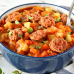Easy Italian Sausage Gumbo in a blue bowl with a spoon next to a kitchen towel and fresh herbs.