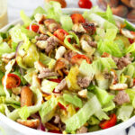 Cheeseburger Salad with Pretzel Croutons in a bowl next to dressing and a bowl of Garlic OMG! Pretzels.