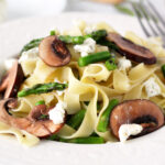 Mushroom Asparagus Pasta with Herb Goat Cheese in a bowl with a fork on the side.
