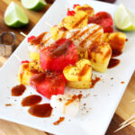 Tajin and Chamoy Fruit Skewers on a plate next to lime slices, heart cookie cutters, and cocktail picks.