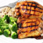 Maple Bourbon Chicken Thighs with a side of brown rice and broccoli on a plate with a fork.