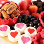 Valentine's Day Snack Board made with Sweet & Salty OMG! Pretzels, strawberries, brie cheese bites, raspberries, chocolate almonds, chocolate coconut, and chocolate covered blueberries on a heart shaped board.