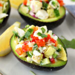 Crab Salad Stuffed Avocados on a plate with fresh cilantro and lemon wedges.