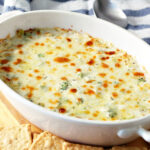 White Pizza Dip with Broccoli in baking dish with crackers and spoons on the side.