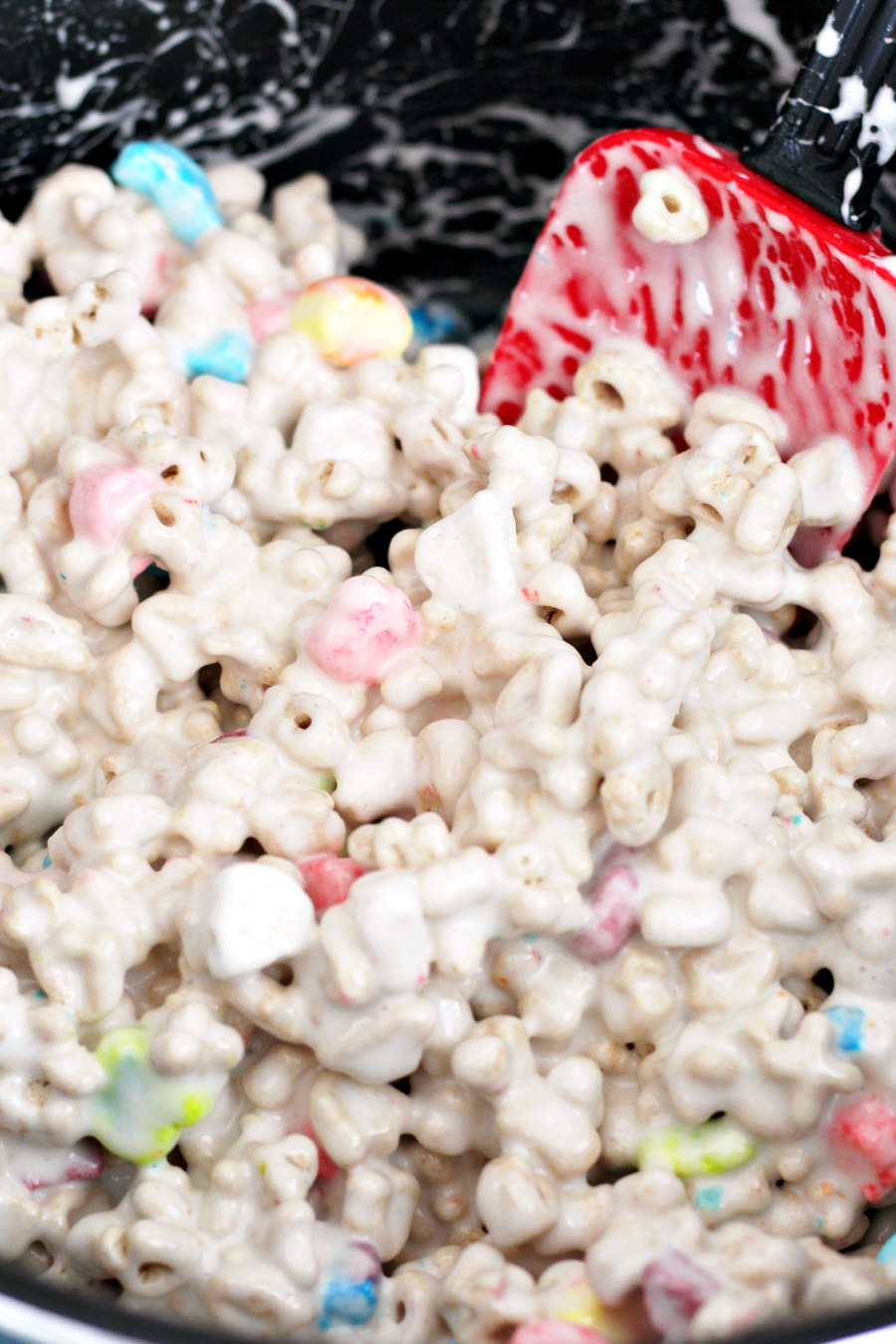 Melted marshmallow and butter stirred with Lucky Charms cereal in a large pot with a rubber spatula.