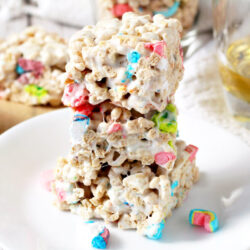 Lucky Charms cereal treats on a plate with a glass of bourbon and Lucky Charms treats on the side.