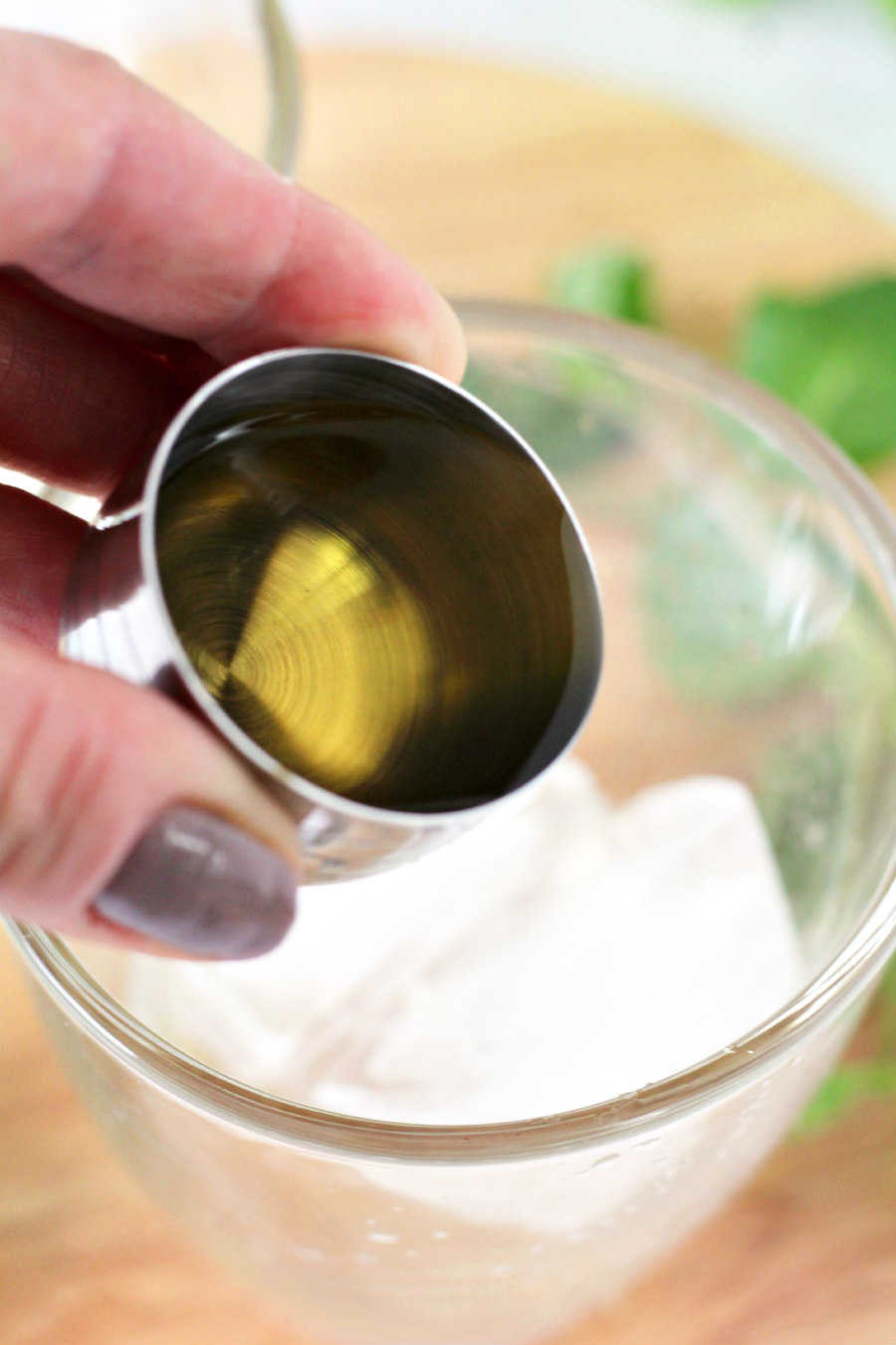 Hand pouring ounce of whiskey into a glass filled with ice.