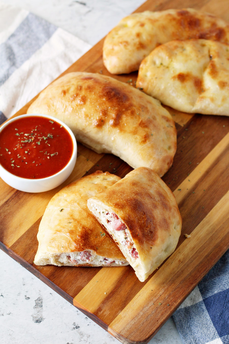 Italian Easter Pie Calzones on a wooden board with a bowl of marinara sauce.