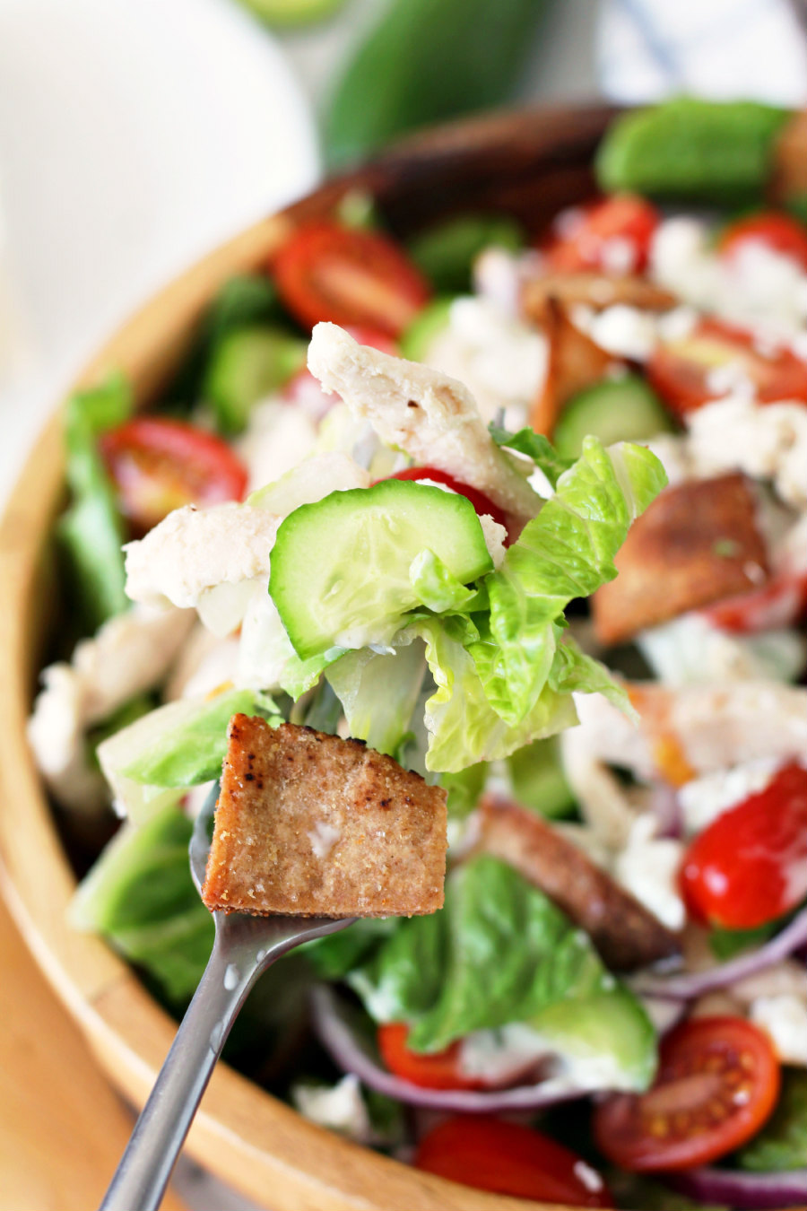 A forkful of Chicken Gyro Salad being held over a wooden salad bowl.