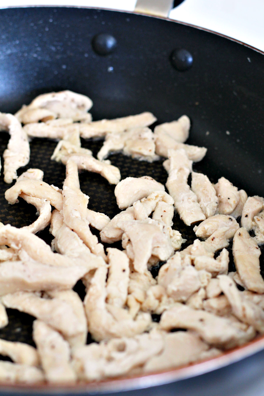 Chicken strips being cooked in a skillet on the stovetop.