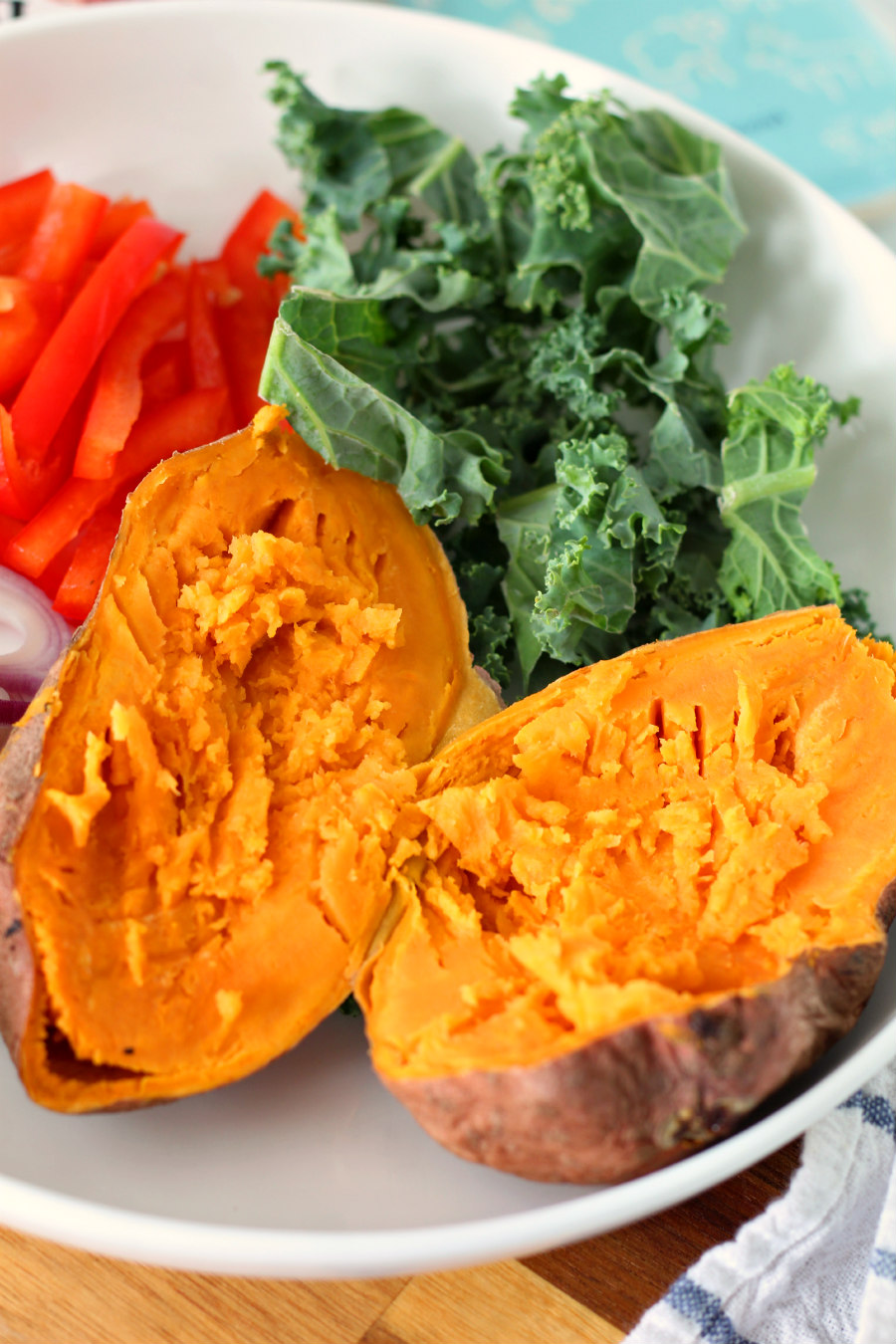 Plate of vegetables including sweet potato, red onion, red bell pepper, and kale.