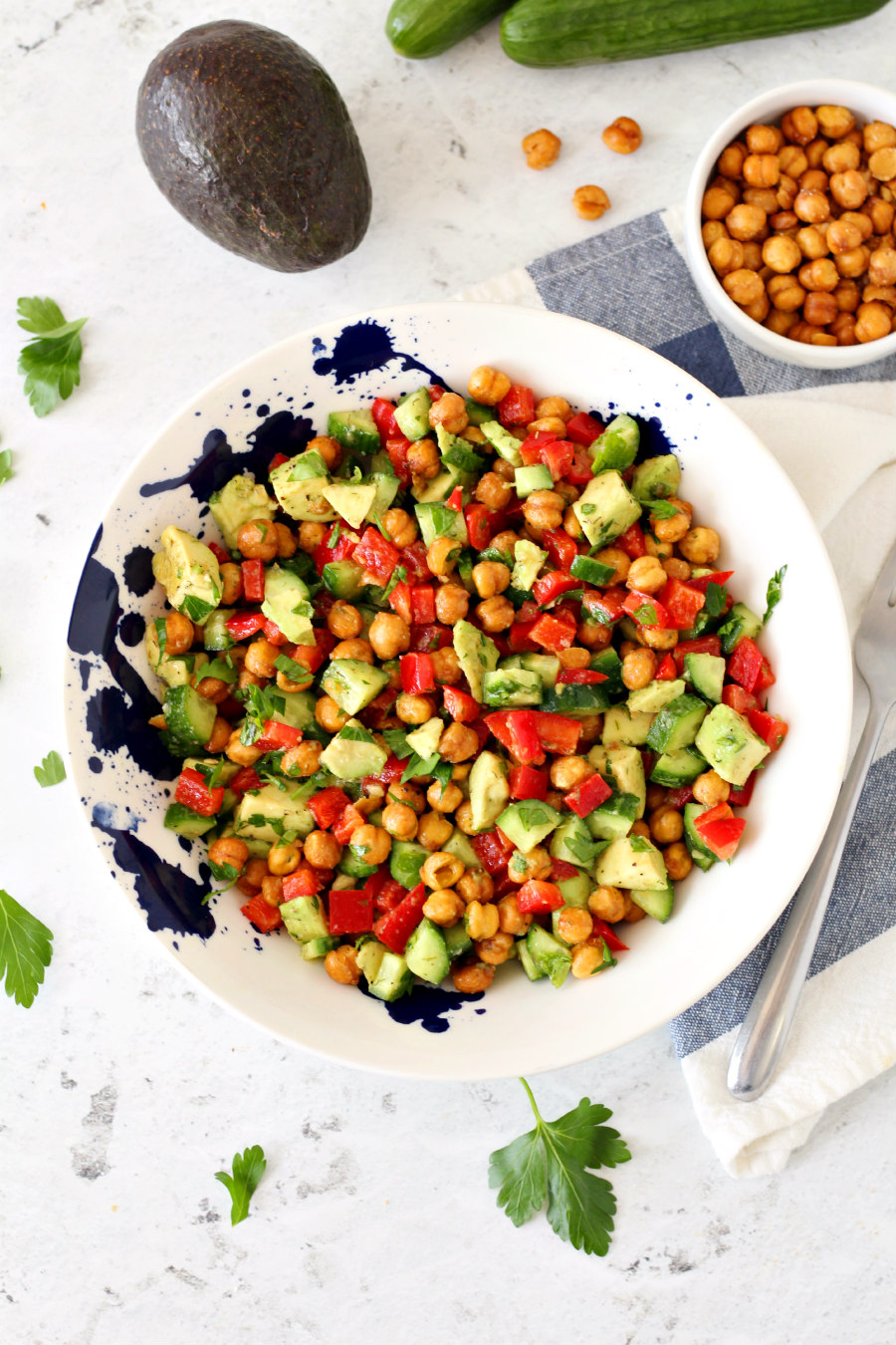 Flat lay photo of Crispy Chickpea and Avocado Salad in a white bowl. Ingredients are spread around the salad bowl.