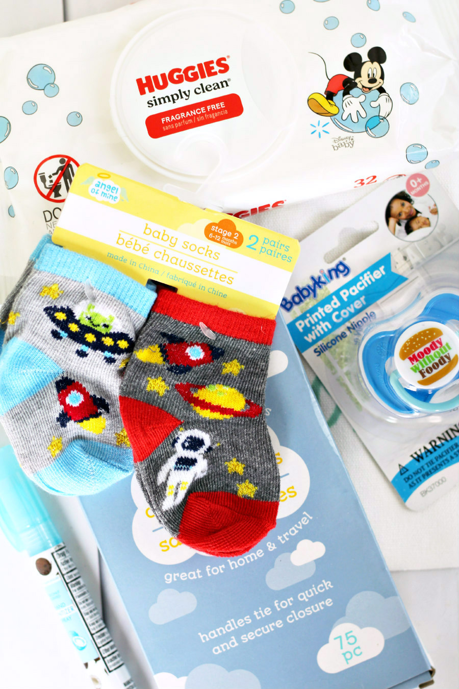 Flat lay photo of Huggies baby wipes, baby socks, hand sanitizer spray, diaper disposal bags, and a pacifier.