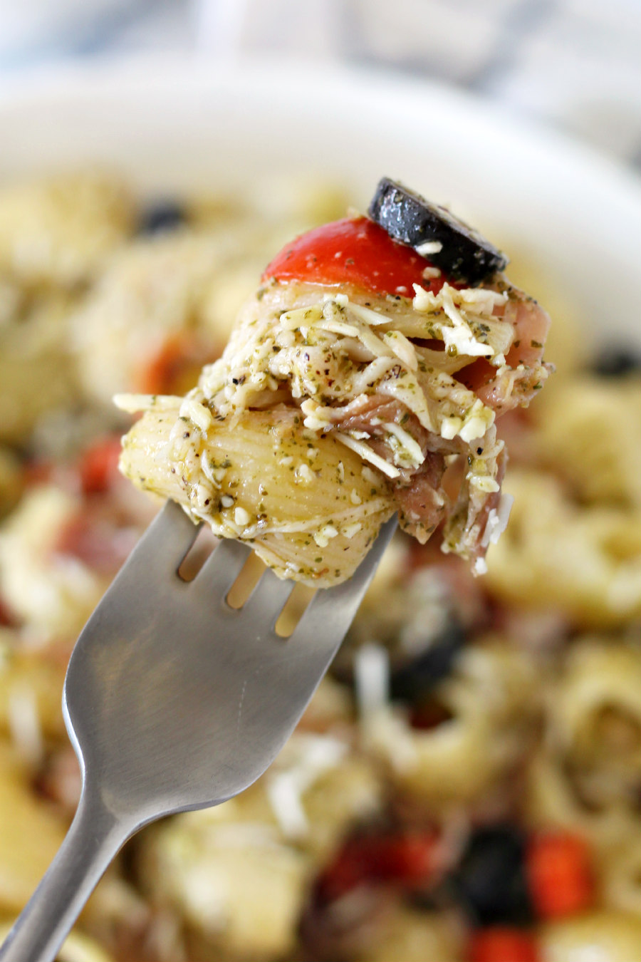 Forkful of Pesto Pasta Salad with Prosciutto being held over serving dish.
