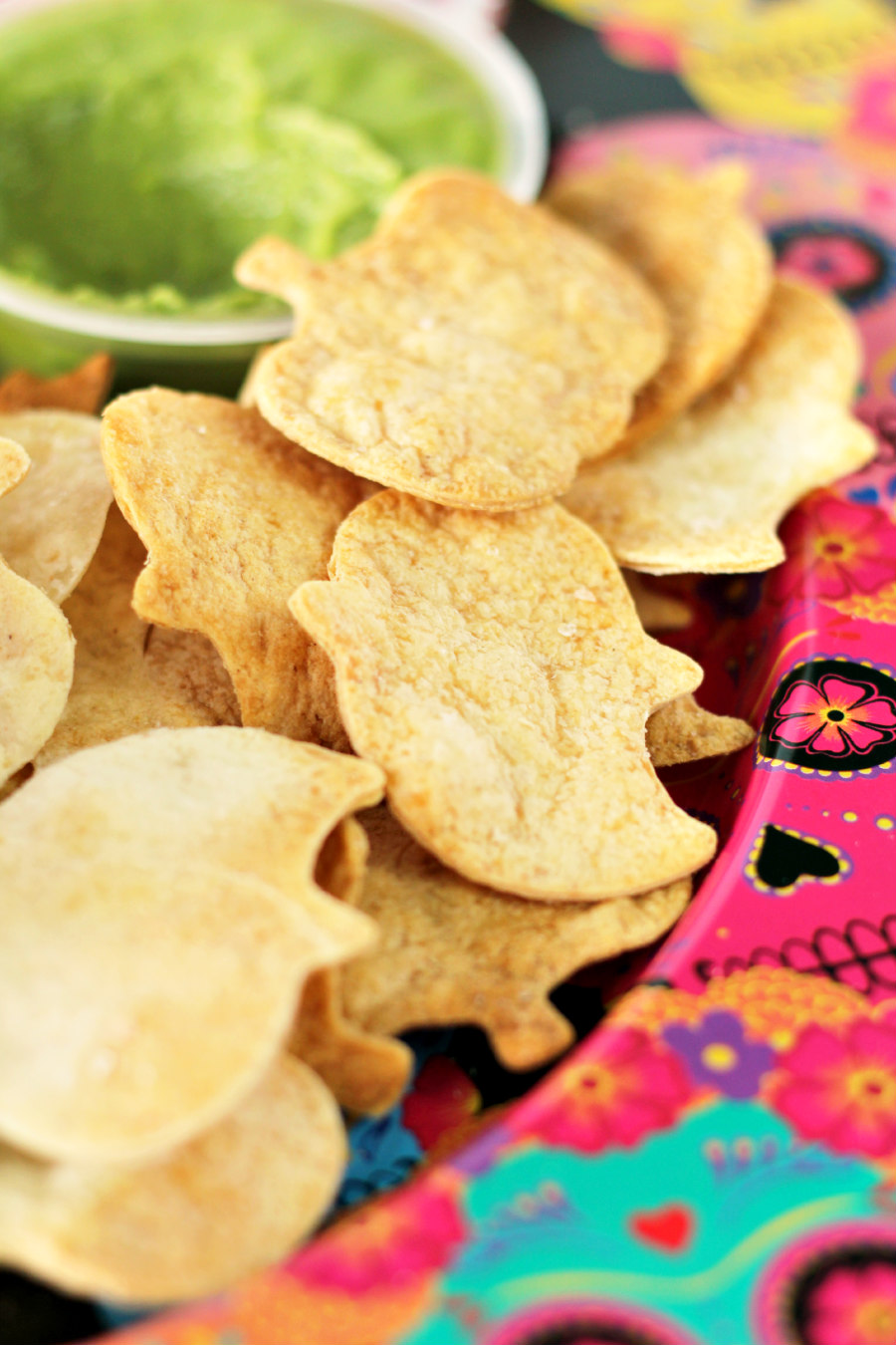 Close up photo of Air Fryer Halloween Tortilla Chips on sugar skull plate with cup of guacamole in the background.