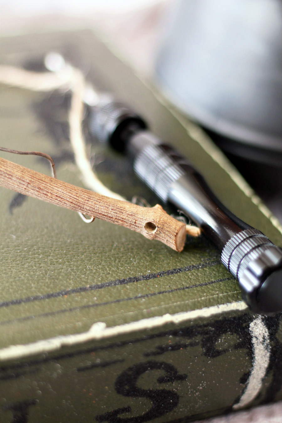 Hole drilled into top of grapevine branch. Hand drill and twine in background along with cauldron and spell book.