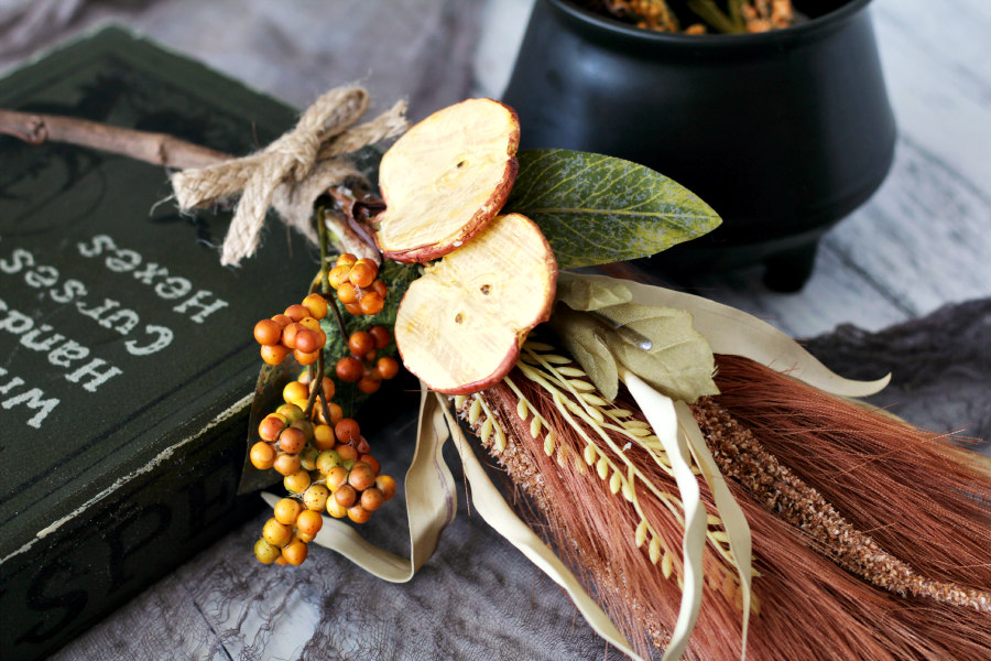 Horizontal photo of Pampas Grass Witch's Broom. Spell book and cauldron also pictured.