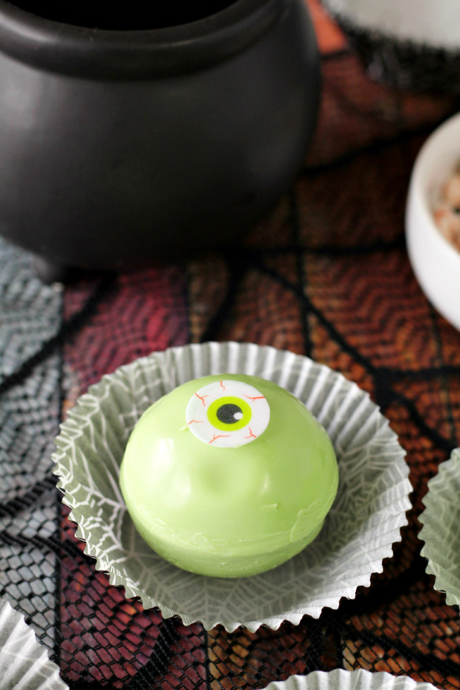 Halloween Eyeball Hot Cocoa Bomb in cupcake liner. Cauldron mug sits in background.