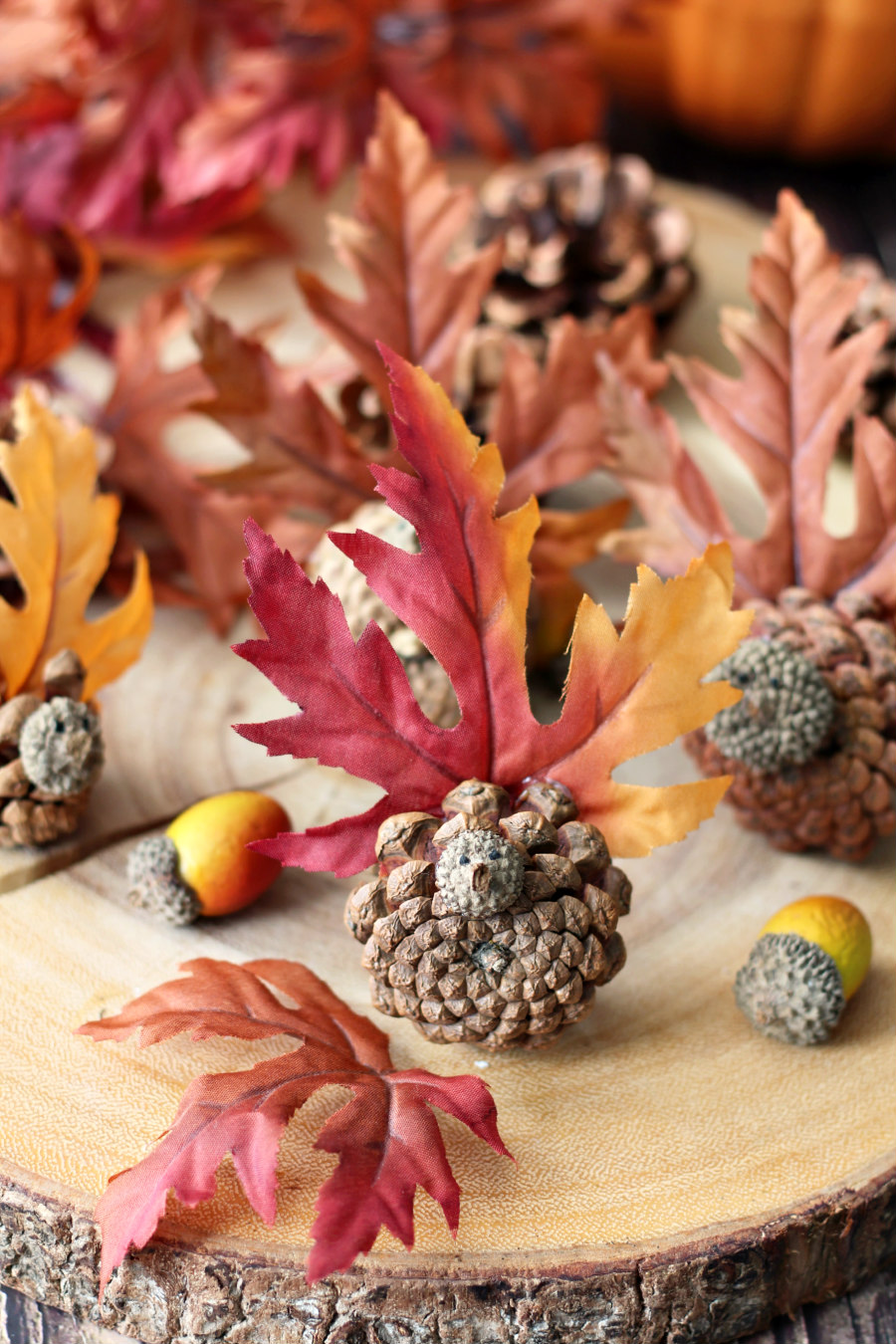 DIY Thanksgiving Pine Cone Turkeys on a wood slice with faux maple leaves, pine cones, and acorns.