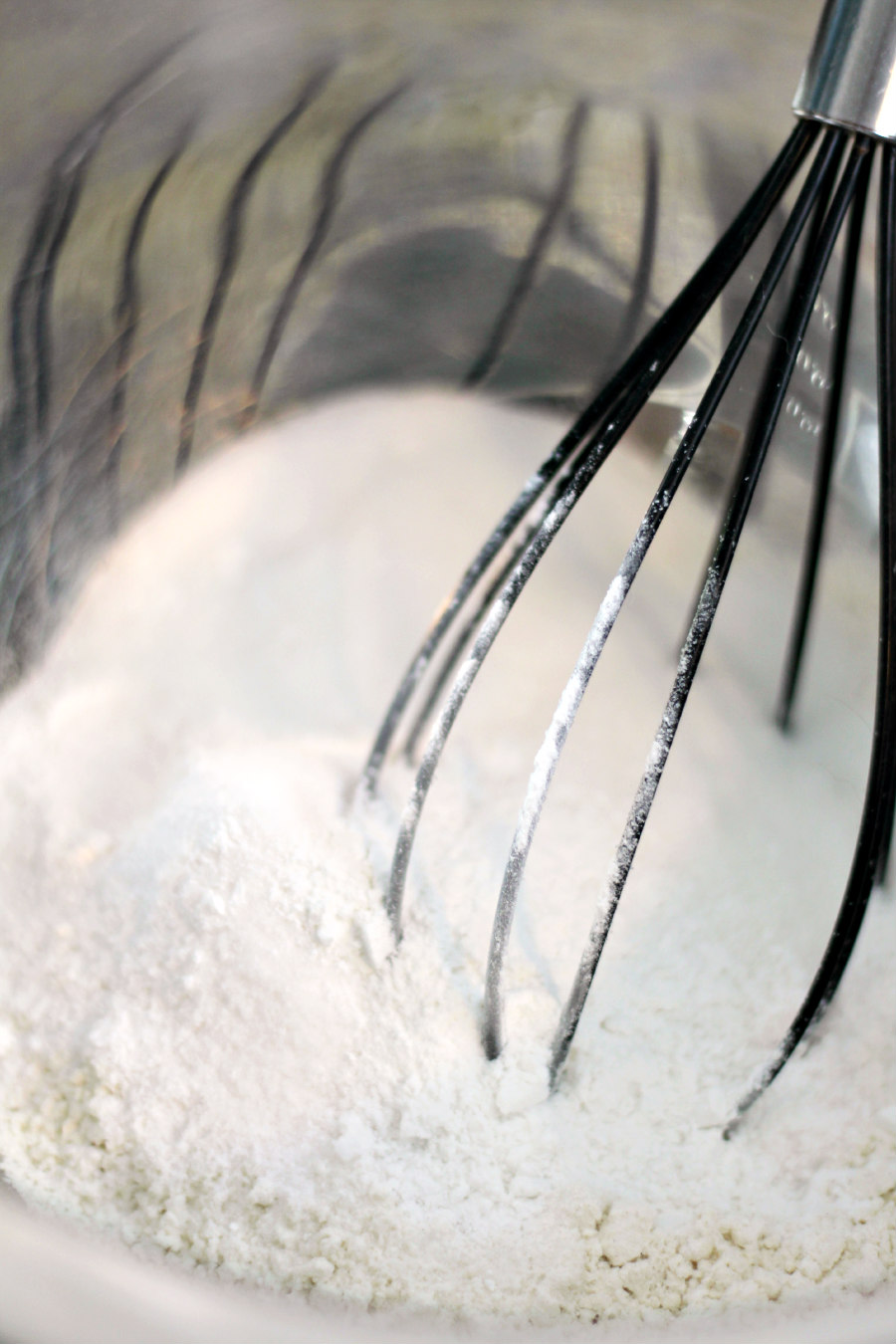 Flour, vanilla pudding mix, sugar, baking powder, and salt with a whisk in a metal mixing bowl.