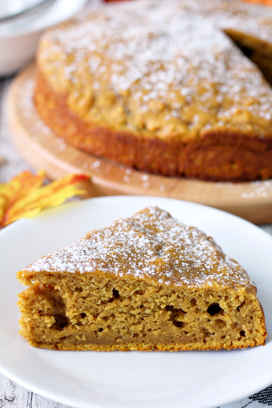 Close up of Pumpkin Spice Ricotta Cake slice in front of cake on wooden board.