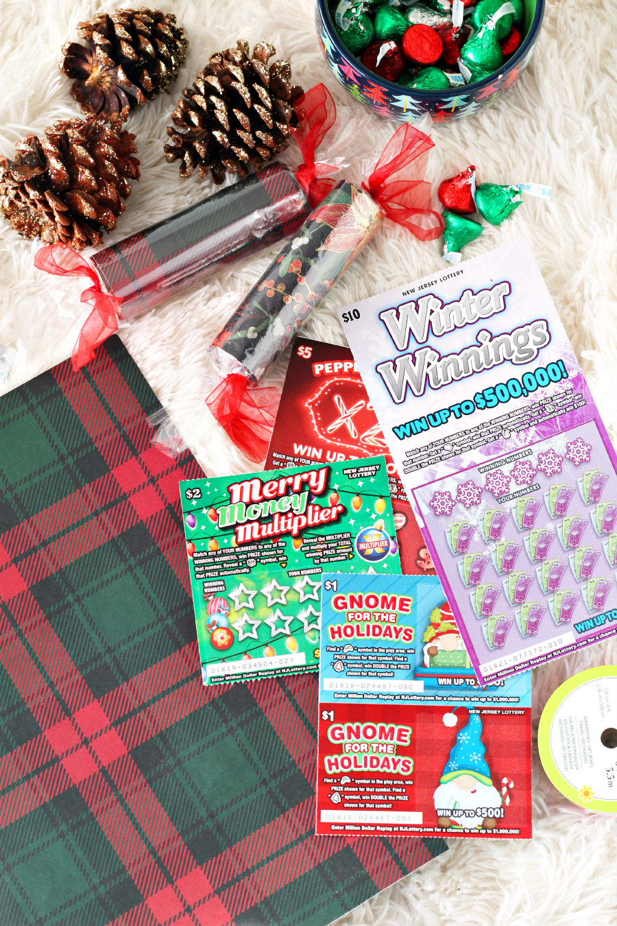 Christmas Candy Lottery Gift Idea pictured with plaid Christmas cardstock, Holiday Scratch-Offs, Hershey Kisses, and sparkly pine cones.