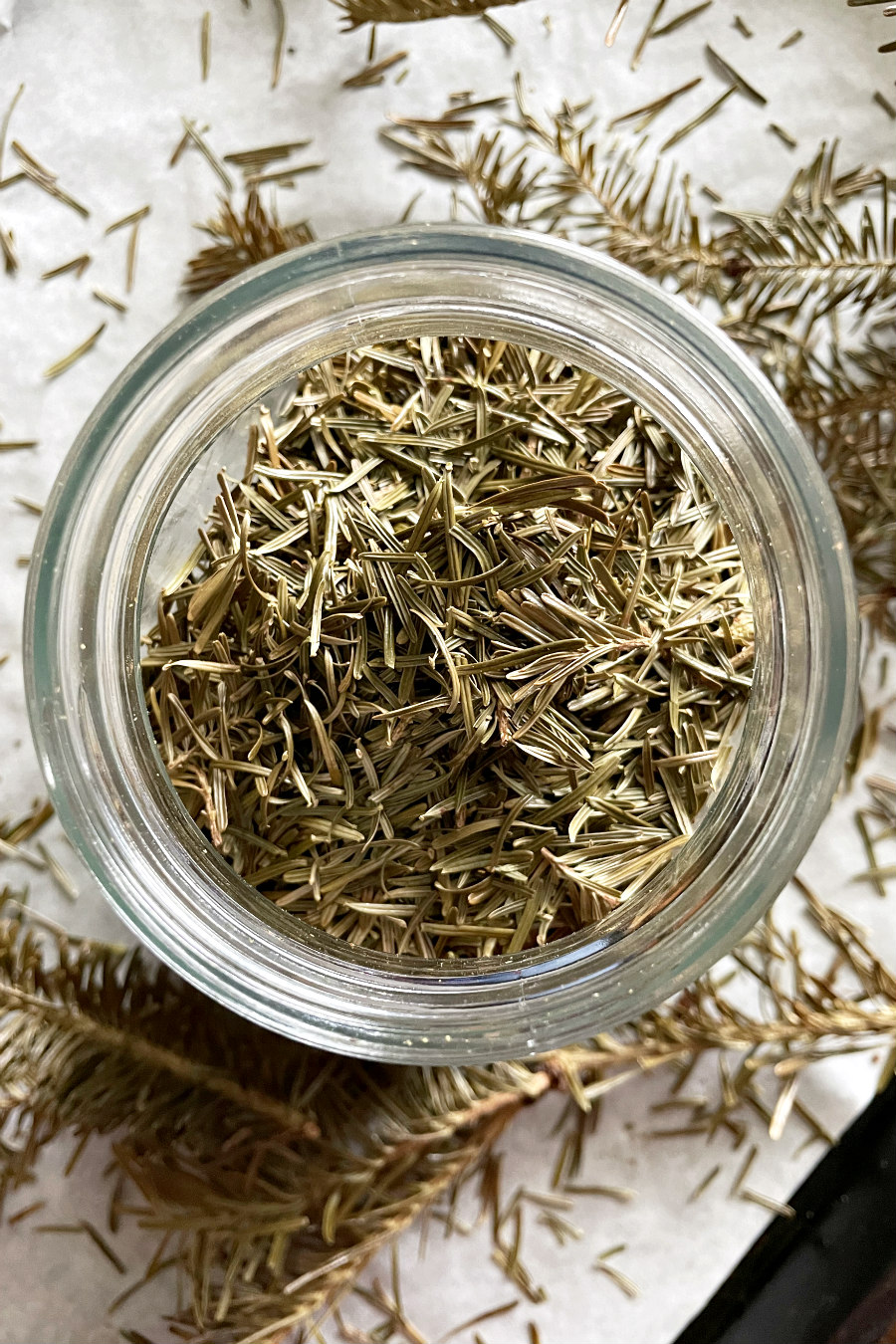 Glass jar filled with fir tree needles on a parchment paper lined baking sheet.