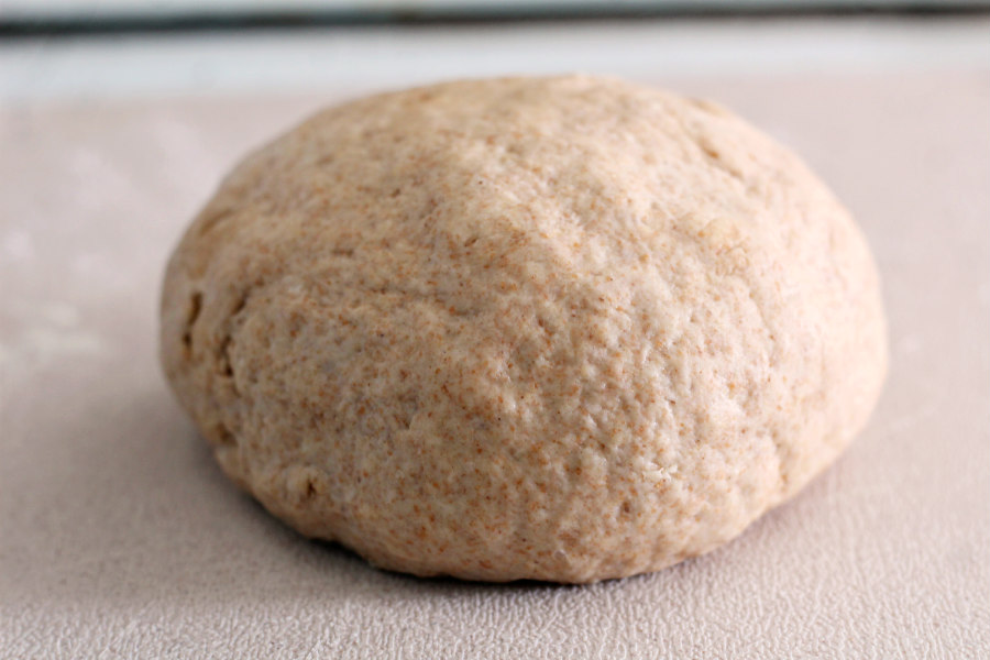Homemade tortilla dough formed into a ball on a lightly floured soil.