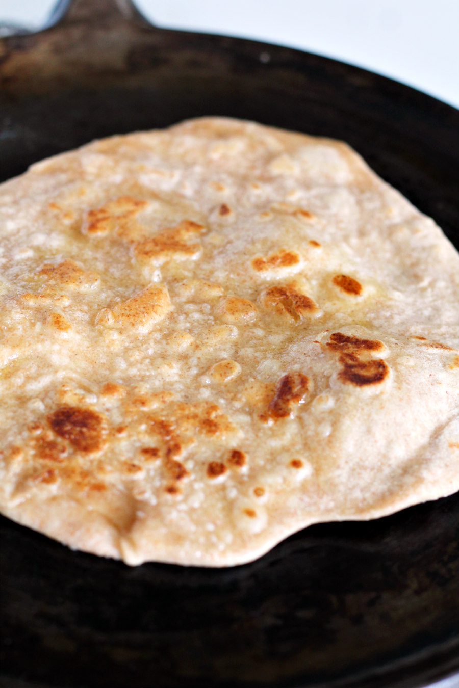 Homemade tortilla being cooked on cast iron griddle pan on stovetop.