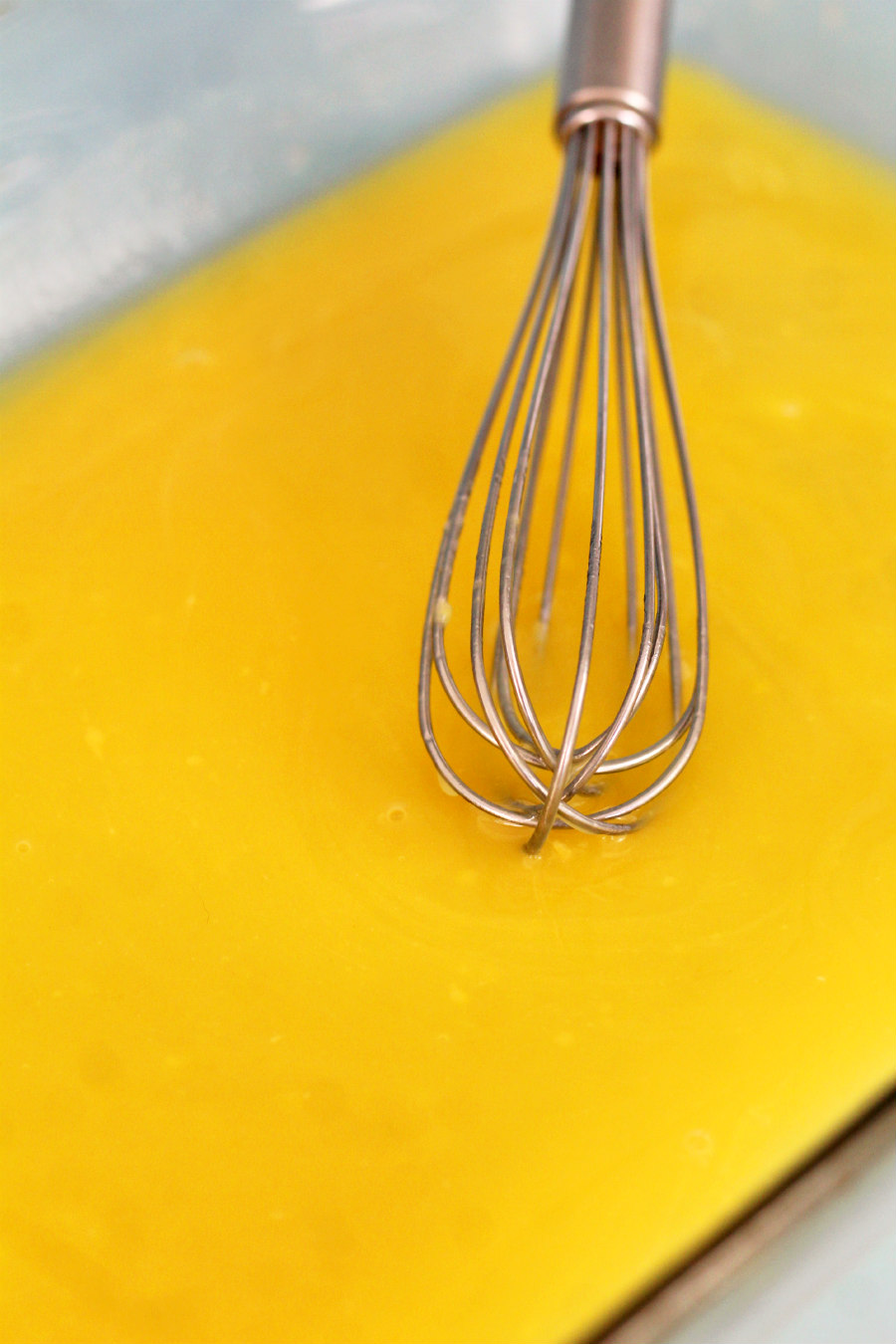Instant banana pudding mix and pineapple juice in baking dish with metal whisk.