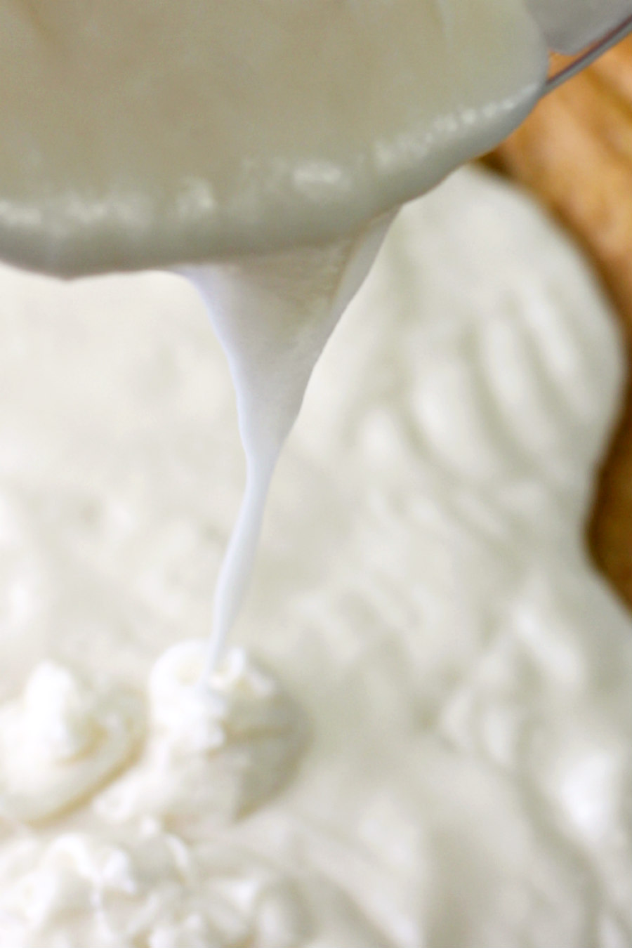 Close up of melted cream cheese frosting being poured over Hummingbird Pudding Dump Cake.