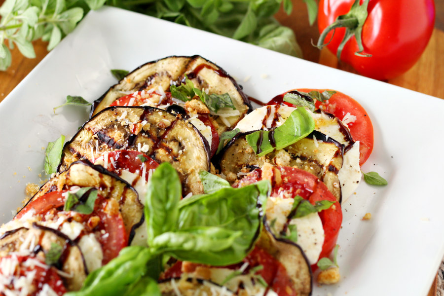 Horizontal photo of Deconstructed Eggplant Parmesan Salad on large white serving platter. Fresh herbs and a tomato sit in background.