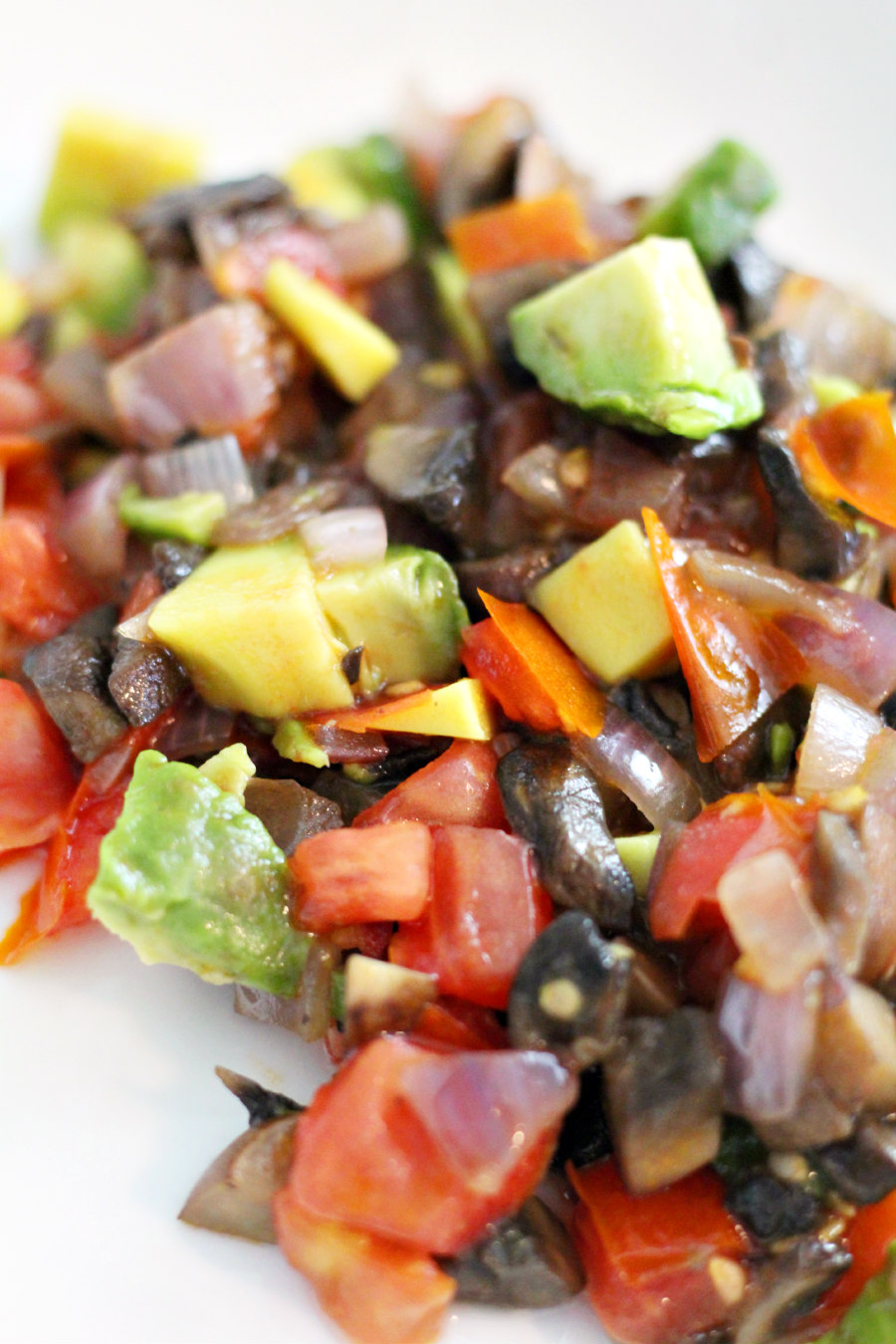 Chopped and cooked baby bella mushrooms, red onion, tomato, and avocado in white plate.