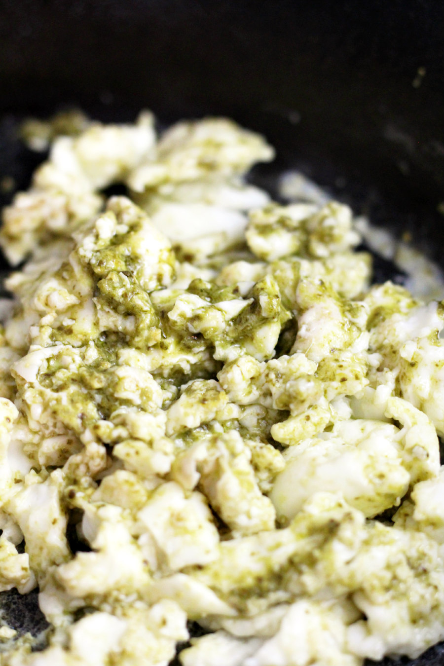 Close up of scrambled egg whites mixed with pesto in cast iron skillet.