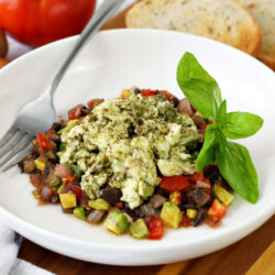 Horizontal photo of Pesto Infused Egg White Skillet served in white dish. Dish sits on top of wooden board. Kitchen towel, tomato, fresh basil, mushrooms, and rye toast also sit in photo.