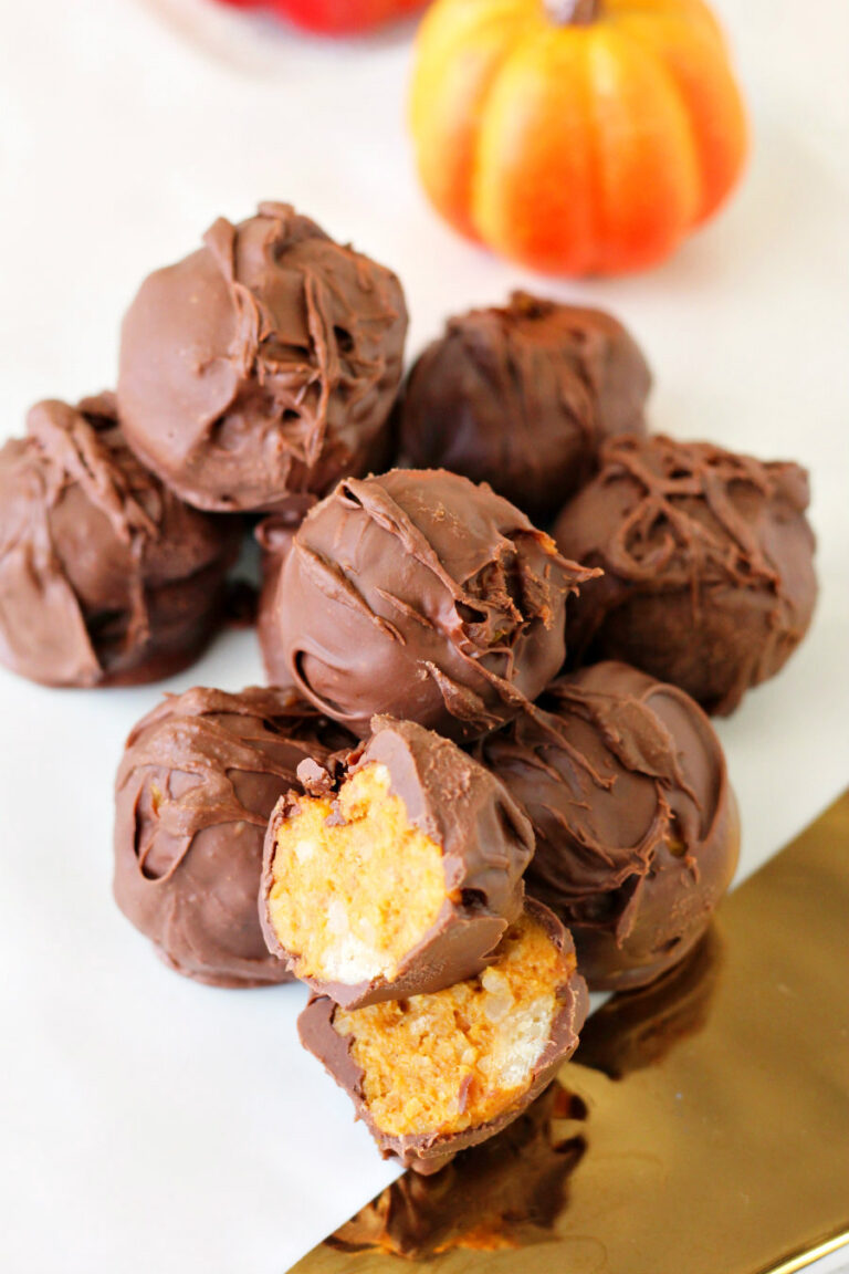 Milk Chocolate Pumpkin Pie Truffles sit in pile on top of white and gold ceramic board. Small pumpkins in partial view in background.