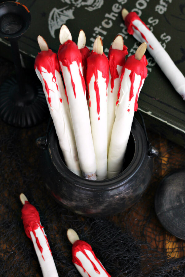 Bleeding Candle Pretzel Rods are displayed in decorative cauldron. Other Bleeding Candle Pretzel Rods, a candlestick holder, and decorative spell book also in partial view.