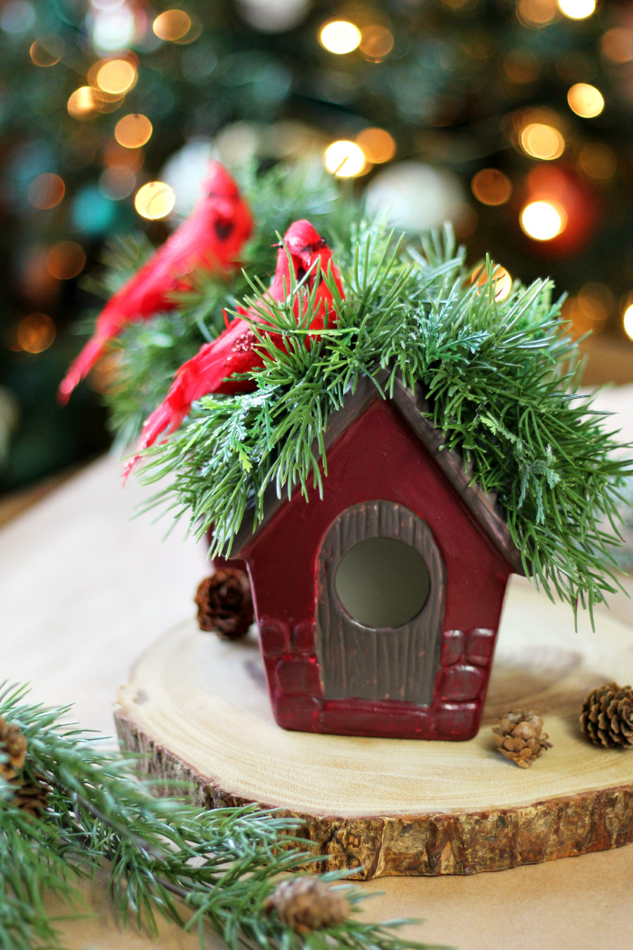 DIY winter birdhouse decorations are displayed on a wood slice on top of kraft paper. Faux greenery also in partial view.