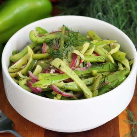 Zesty Sweet Pepper & Dill Salad in white serving bowl sits on wooden board. Fork, pepper, and fresh dill also in partial view.