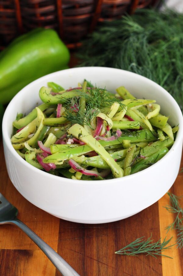 Zesty Sweet Pepper & Dill Salad in white serving bowl sits on wooden board. Fork, pepper, and fresh dill also in partial view.